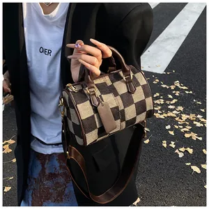 Detail of checkered canvas boston bag with brown leather handles and wide shoulder strap