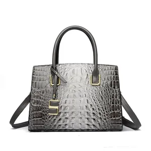 Gray crocodile texture handbag with gold hardware and shoulder strap on white background