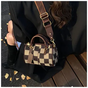 Classic checkered Boston bag with wide canvas strap shown in use on a wooden bench