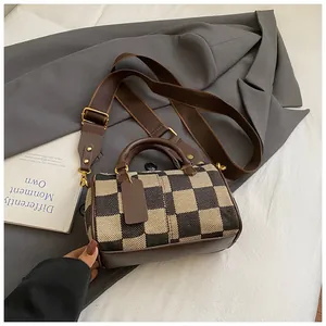 Close-up of canvas checkerboard pillow bag with wide strap and brown leather details