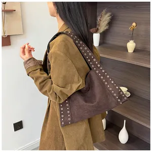 Détail d'un sac porté épaule en daim marron foncé avec œillets métalliques et bandoulière