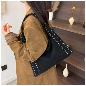 Détail du sac bandoulière noir à rivets avec œillets porté par un mannequin en veste