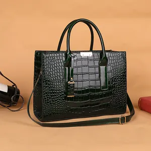 Borsa a mano verde scuro a motivo coccodrillo, dettagli dorati e manici su sfondo beige