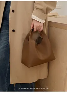 Detalle de un bolso tipo cubo de cuero marrón con patrón de lichi y asa de estilo retro