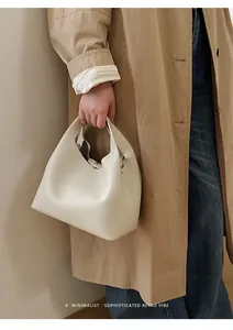 Detalle del bolso de cubo crema mostrando textura de cuero granulado y el cierre metálico