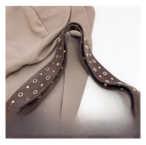 Détail d'une large bandoulière en daim marron avec œillets métalliques dorés et rivets