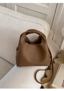 Detalle del bolso cubo de cuero granulado marrón sobre un sofá de tela crema