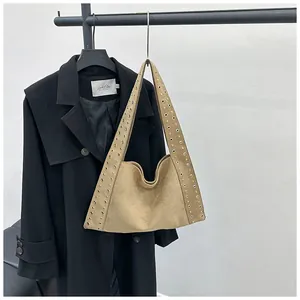 Gros plan du sac hobo en daim camel avec rivets dorés suspendu sur un cintre noir
