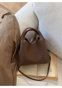 Detalle de bolso tipo cubo en cuero marrón oscuro con asa superior y correa de hombro
