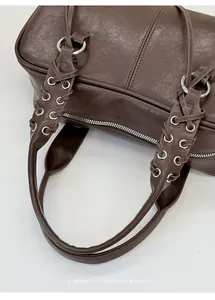 Detail of dark brown leather handbag featuring silver metal rings and woven strap handle