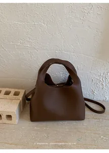 Detalle del bolso de cubo en cuero marrón granulado con hebilla de metal y asa redonda