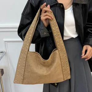 Sac bandoulière en daim marron avec rivets dorés porté par un mannequin femme