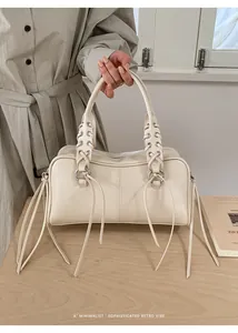 Detail of cream leather pillow bag with braided handles, metal eyelets and long tassels