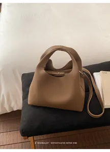 Detalle de bolso cubo de cuero marrón con textura granulada y correa de hombro ajustable