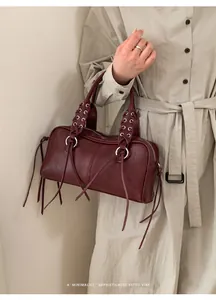 Close-up of a burgundy leather baguette bag with retro tie details and metal eyelets