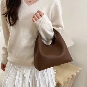 Bolso tipo cubo minimalista de cuero marrón oscuro con suéter crema y falda blanca larga