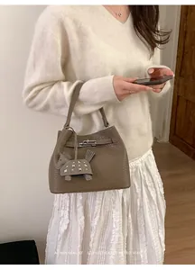 Detalle del bolso tipo cubo de cuero marrón con patrón de litchi y cierre plateado