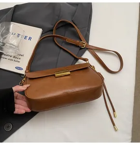 Detail view of caramel crossbody bag with gold buckle on a stylish suit backdrop