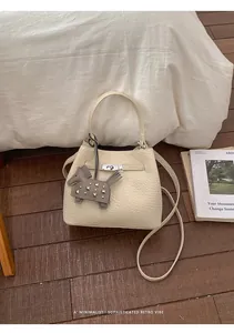Detalle de bolso bucket crema en piel granulada con cierre giratorio plateado