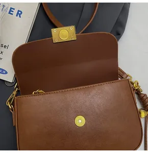 Detail of a brown leather crossbody bag with golden magnetic clasp and textured hardware
