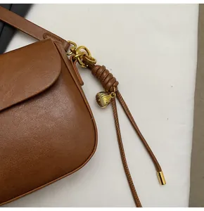 Detail of retro brown leather bag with golden shell charm and knotted strap accent