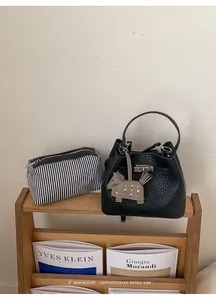 Detalle de bolso bucket de cuero negro con cierre plateado y estuche a rayas