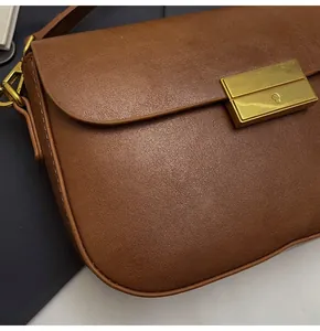 Close-up of brown litchi grain leather texture and golden rectangular metal clasp detail