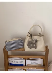 Vista de detalle del bolso tipo cubo de cuero crema con bolsa interna a rayas y adorno