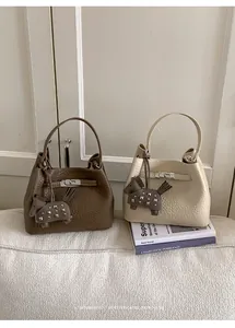 Detalle de dos bolsos tipo cubo minimalistas en marrón y beige con colgantes