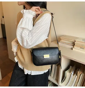 Detail of black leather crossbody bag with gold buckle and woven charm on a model
