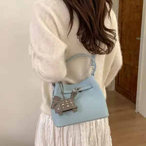 Bolso cubo azul claro de piel granulada con cierre giratorio y colgante de caballo gris