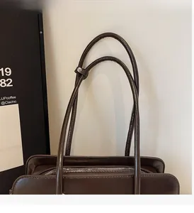 Detail of reinforced handles and silver metal zipper on dark brown oil wax leather bag