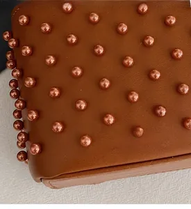 Detailed close-up of brown leather bag with elegant matching pearl studs