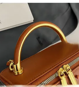 Close-up of brown leather bag with golden double zippers and curved top handle detail