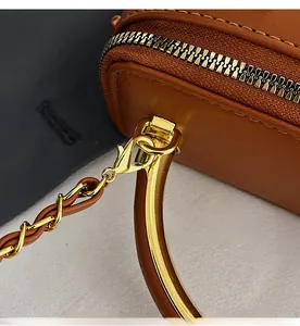 Close-up of brown leather bag with golden hardware, zipper detail and detachable chain hook