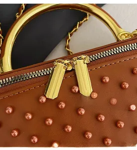 Detail of smooth gold double zippers and pearl embellishments on a brown leather handbag
