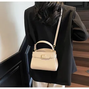 Détail du sac à main en cuir beige avec boucle dorée sur une veste de blazer noire
