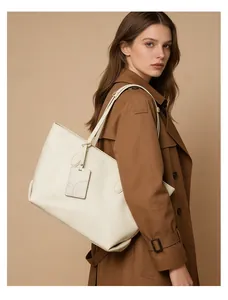 Detailed view of cream leather tote bag with branded tag on a stylish trench coat