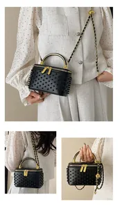 Detail of black box bag with circular studs, gold metal handle and chain strap