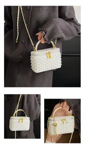 Detail of white faux pearl box bag featuring gold metal handle and chain shoulder strap