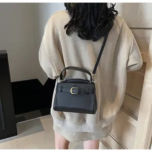 Détail d'un sac bandoulière en cuir noir avec boucle dorée sur pull en maille beige