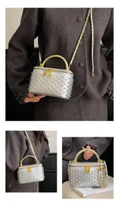 Close-up of silver box bag with pearl studs, gold handle and woven chain strap details