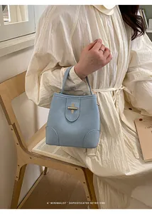 Detail of light blue suede bucket bag with a metal cross-lock closure and short handle