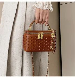Detail of brown leather box bag with stud texture and gold chain strap charm