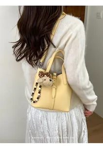 Detail of pale yellow bucket bag featuring pebble leather and cute plush bear charm