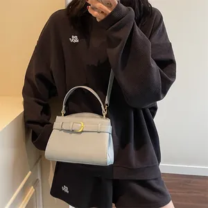 Sac à main de luxe gris clair en cuir texturé avec bandoulière porté par un mannequin
