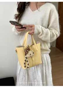 Detail of yellow pebbled bucket bag with cute plush bear charm and bow tie accessory