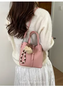 Pale pink bucket bag with leather strap and plush bear charm shown on a model's shoulder