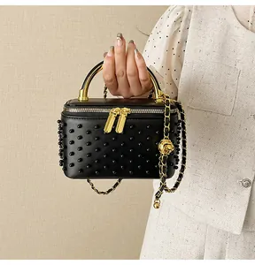 Detail of black box bag with bead embellishments, gold handle, and adjustable chain strap