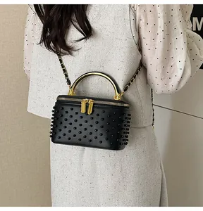 Detail of black cylinder box bag with metallic rivets and golden handle worn by model